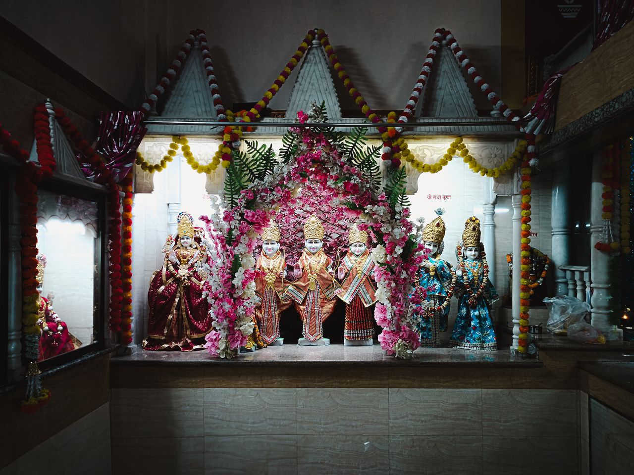 A beautifully decorated temple shrine showcasing intricate Hindu deity statues surrounded by vibrant floral garlands and ornaments.