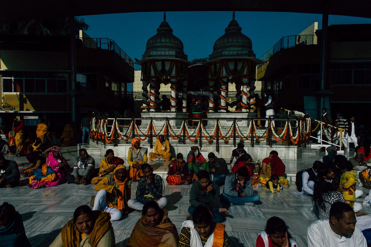 Pensive Indian people in traditional clothes sitting on floor in temple and praying on sunny day